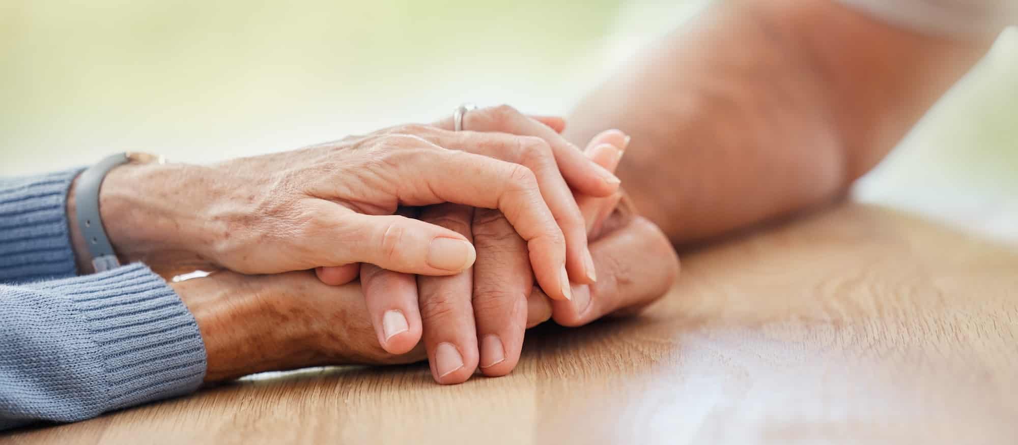 Senior, holding hands and support with couple, comfort and help on table for grief, pain or sympath