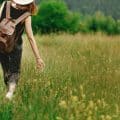Stylish hipster woman walking in grass and holding in hand herb wildflowers
