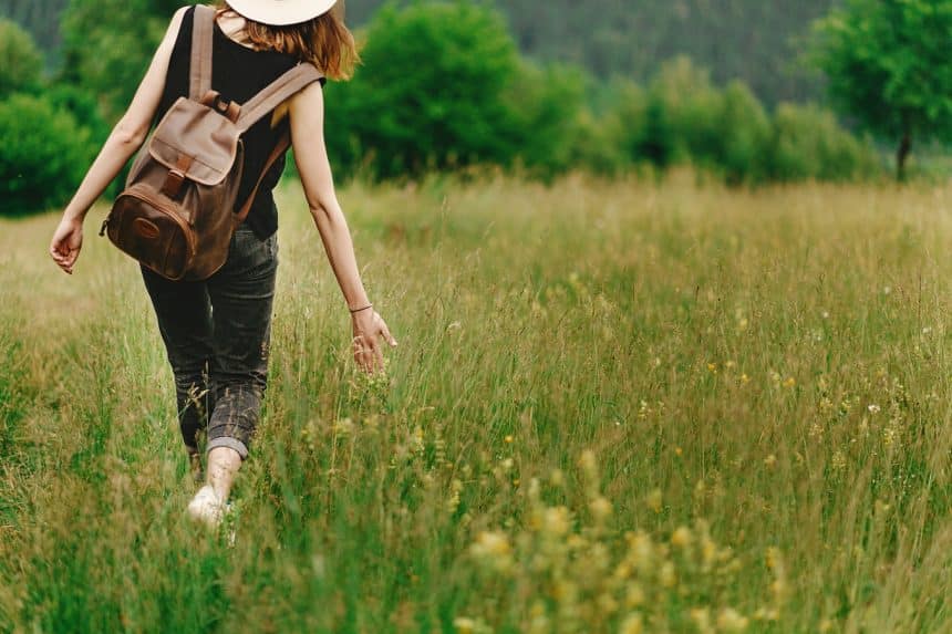 Stylish hipster woman walking in grass and holding in hand herb wildflowers