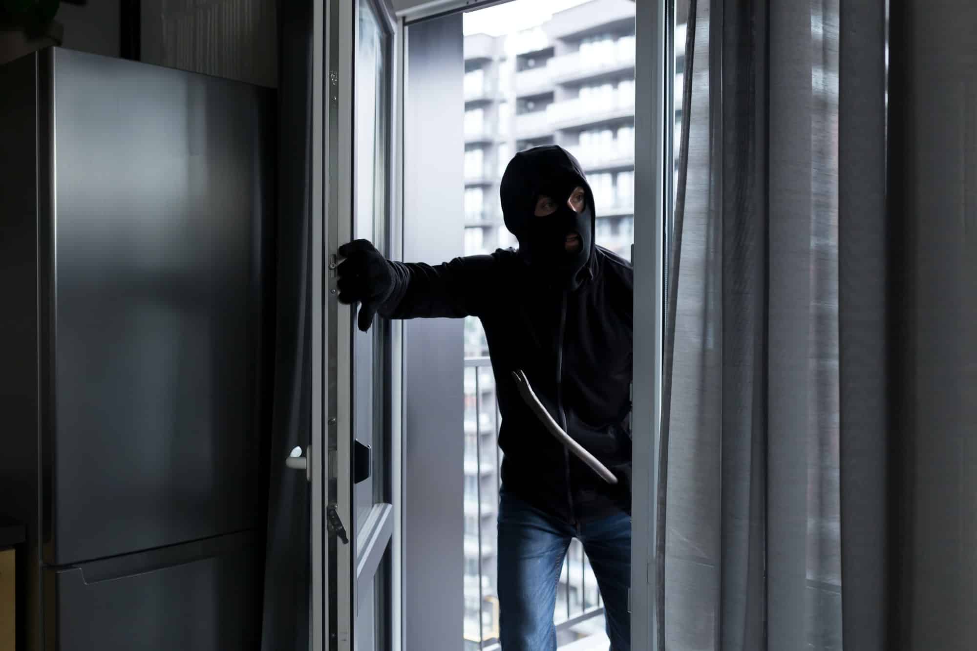 A male thief in a black mask, enters the apartment for robbery, the robber broke the door lock