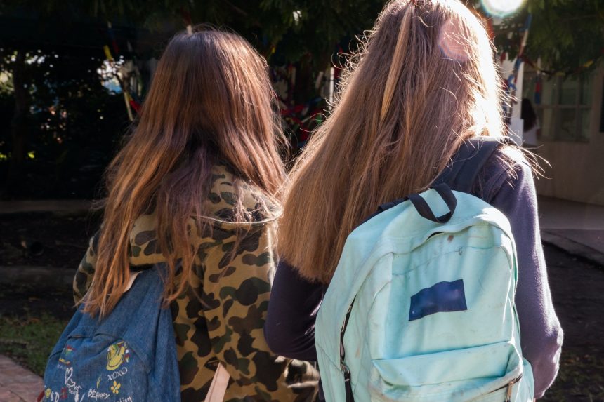 Two high school girls walking into school with backpacks